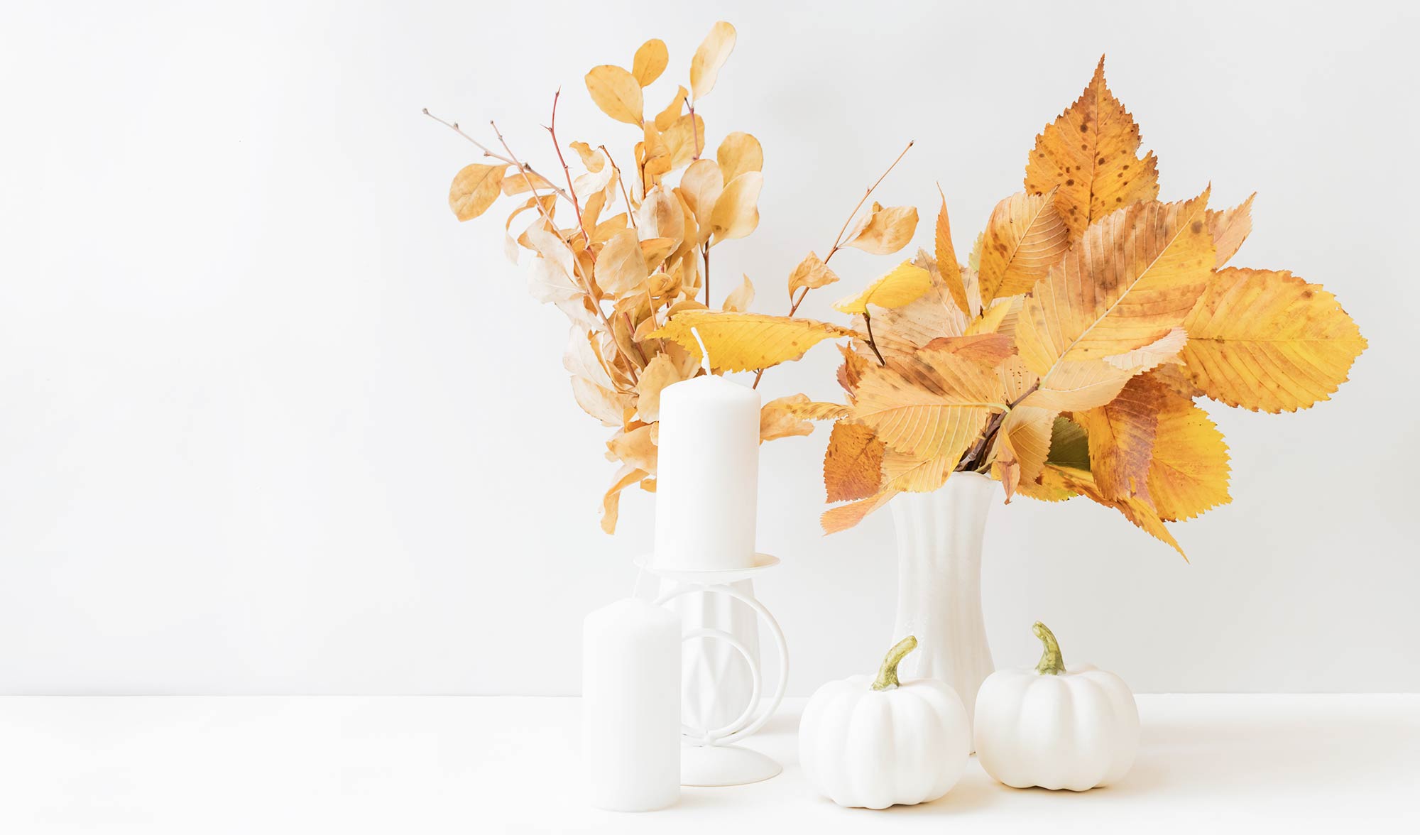 White candles and pumpkins with fall leaves 