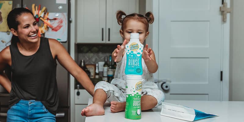 mom smiling at toddler holding Lemi Shine product 