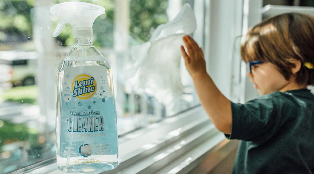 little boy cleaning window next to bottle of glass cleaner 