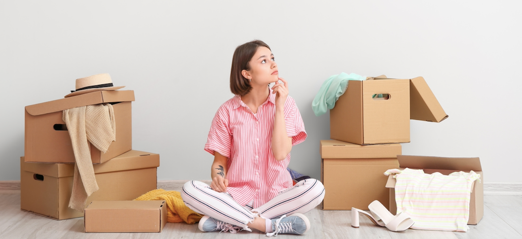 Girl sitting on floor, thinking about decluttering her home. She is surrounded by boxes 