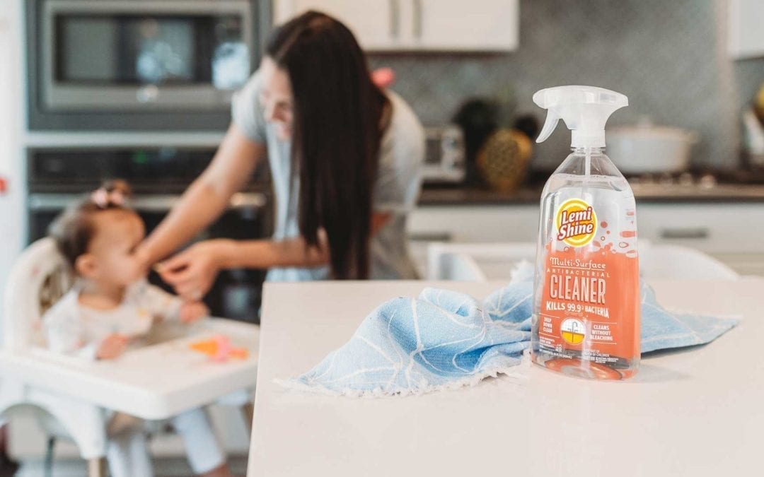 close up of spray on kitchen counter, mother feeding daughter in background 