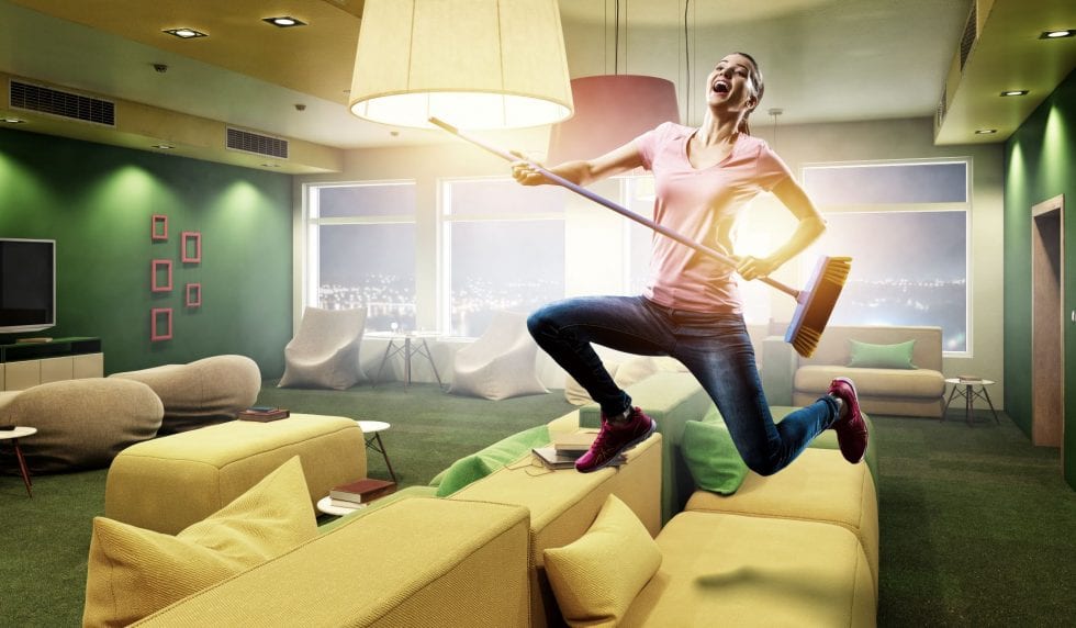 woman leaping over couch with broom in hand 