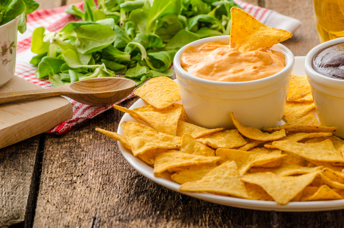 a tabletop with a bowl of chips and nacho cheese 