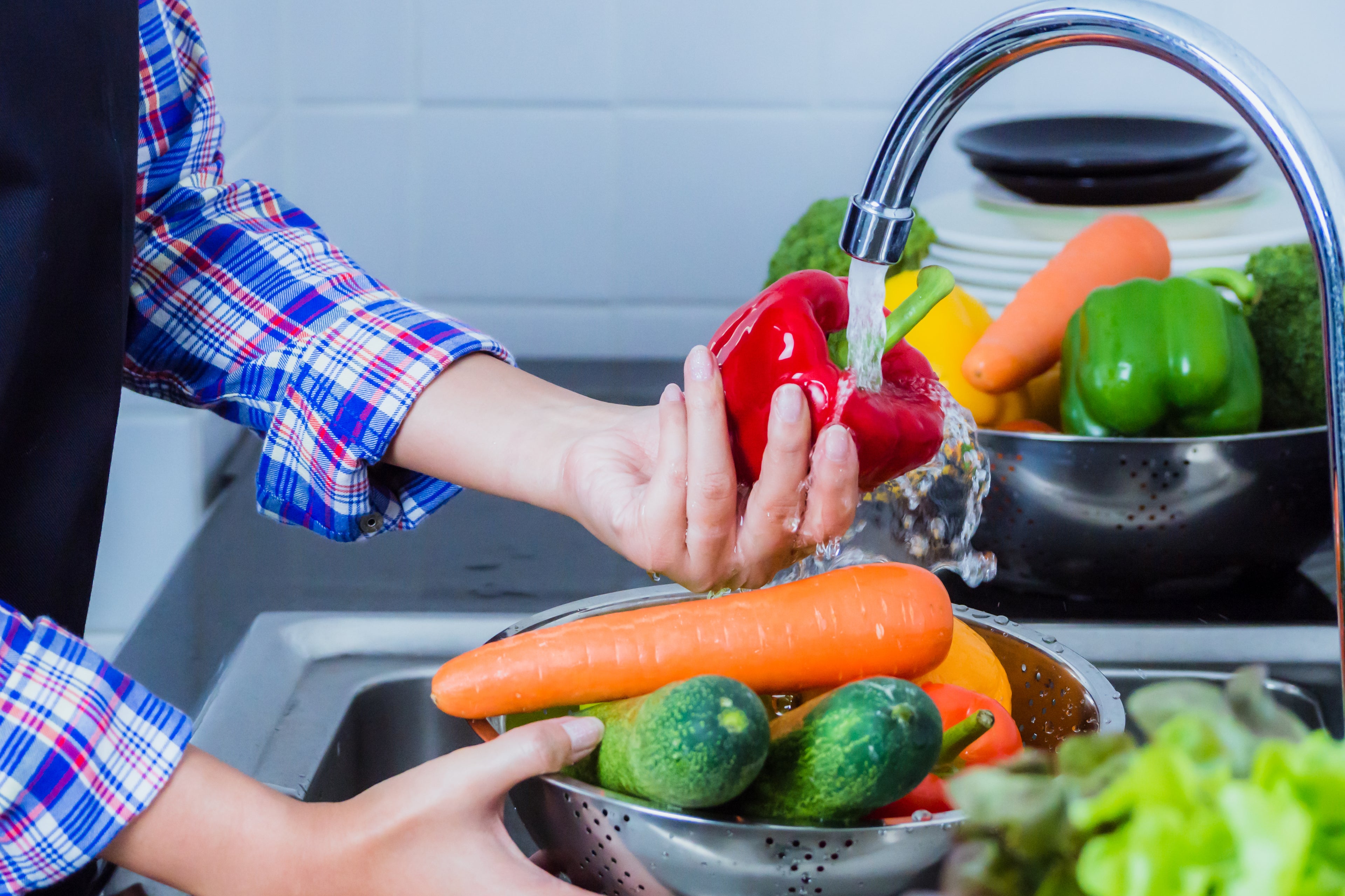 person washing produce in sink with running water 